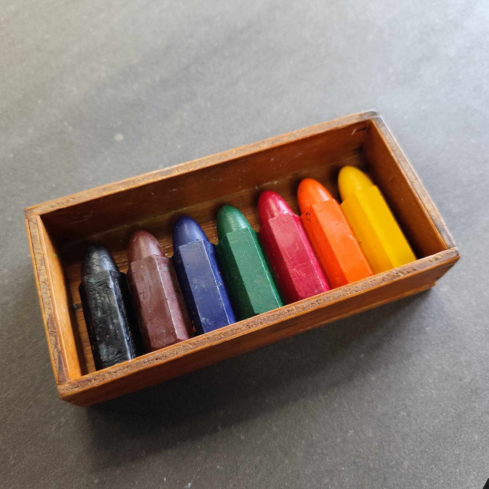 Seven hexagon crayons from black to yellow in a small wooden box